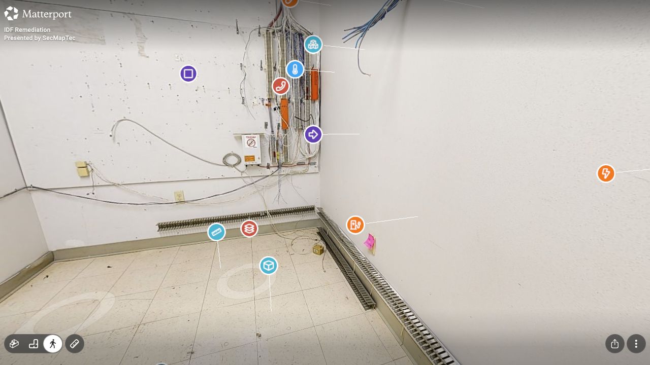 Interior view of the communication room with color-coded remediation tags beside the existing cabling, backboard, and floor area